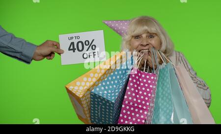Iscrizione fino al 40% di sconto appare accanto alla nonna sorridente. Donna anziana con borse per la spesa festeggiando, ballando, cercando soddisfatto con prezzi bassi, sconti, shopping su Black Friday Foto Stock