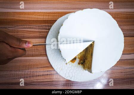 Vista dall'alto di una persona che taglia una torta con bianco glassa Foto Stock