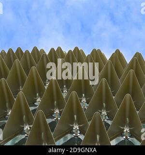 Vista ravvicinata di file di triangoli d'oro metallizzato ripiegati su uno sfondo blu del cielo. Foto Stock
