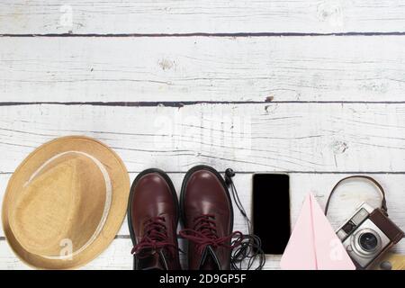 Ancora vita di vestiti con cappello, piano di carta, vecchia macchina fotografica, su uno sfondo di legno bianco Foto Stock