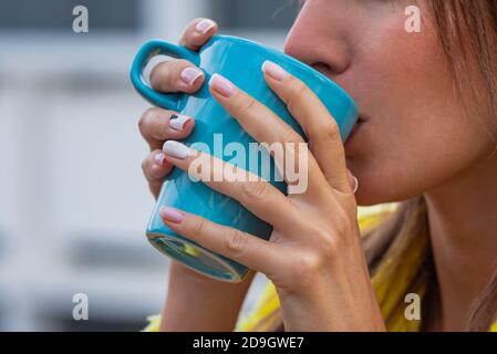 Giovane donna che beve tè o caffè verme da una tazza blu. Foto Stock