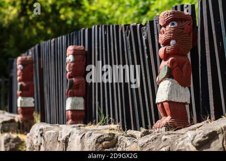 Una fila di sculture Maori tekoteko (figura umana) neozelandesi lungo una recinzione. Messa a fuoco selettiva sulla figura in primo piano Foto Stock