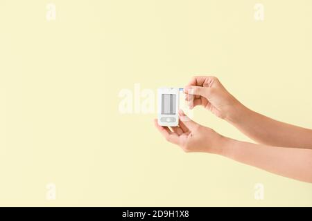 Mani femminili con glucometro su sfondo colorato. Concetto di diabete Foto Stock