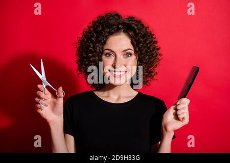 Foto di bella ragazza sorriso mani tenendo forbici pennello pronto per il taglio isolato su sfondo rosso brillante Foto Stock