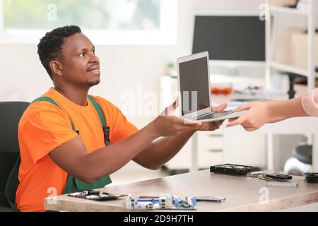 Tecnico afro-americano che fornisce un computer portatile fisso al proprietario del centro di assistenza Foto Stock