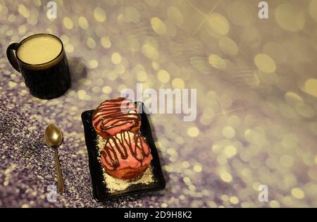 Due ciambelle in smalto rosa e una tazza di cappuccino su sfondo grigio lucido. Primo piano. Foto Stock