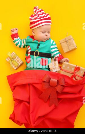 Dormire bambino piccolo in costume di elfo e con regali di Natale su sfondo a colori Foto Stock