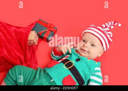 Carino bambino piccolo in costume di elfo e con regali di Natale su sfondo a colori Foto Stock