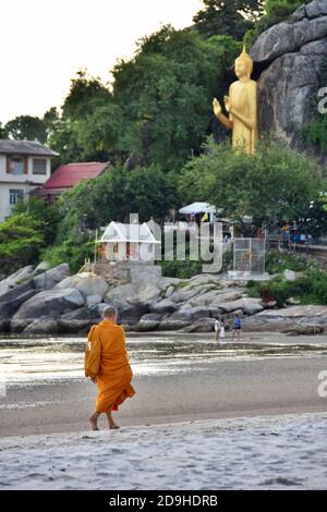 Il monaco buddista camminando sulla spiaggia di sabbia di ritorno verso il tempio Khao Takiab al mattino. Il simbolo della statua del Buddha d'oro è sullo sfondo. Foto Stock