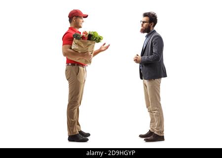 Foto di profilo a lunghezza intera di un corriere di consegna con un borsa della spesa che parla con un cliente maschile bearded isolato sopra sfondo bianco Foto Stock