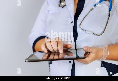 Medico femminile che usa un tablet digitale mentre si sta in piedi vicino alla scrivania presso la clinica di emergenza medico ospedaliero al lavoro. Foto Stock