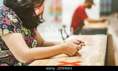 Donna che usa telefoni cellulari per lavorare con immagine sfocata di il contrassegno di posto alternativo per la distanza sociale regola la distanza per uno sedile da altre persone a. Foto Stock