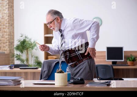 Anziano dipendente che soffre di radicolite sul posto di lavoro Foto Stock