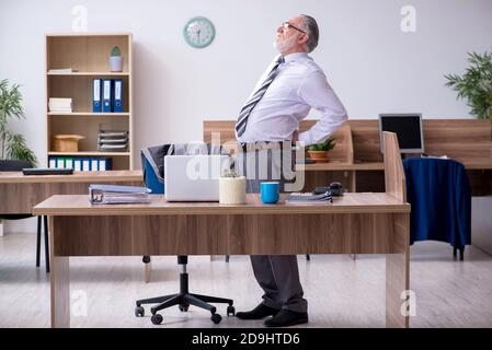 Anziano dipendente che soffre di radicolite sul posto di lavoro Foto Stock