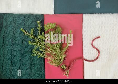 tessuti nei colori rosso, verde e bianco. tradizionali tonalità natalizie per abbigliamento a maglia e ramo di albero di natale con nastro rosso. abiti invernali e di vacanza. Foto Stock