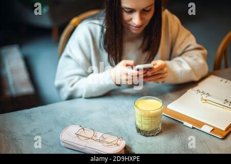 Giovane caucasica sorridente e tenente un bicchiere di caldo latte curcuma sul tavolo Foto Stock