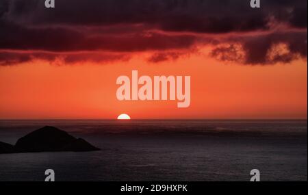 Bellissimo tramonto in rosso e viola sul mare sotto le nuvole dalle forti tempeste. Orizzonte che tocca il sole. Foto Stock