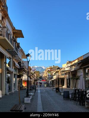 Strada tipica di Chania, Creta, Grecia con negozi, caffè e ristoranti per la passeggiata serale. Nessun turista, mattina presto. Neve sulle montagne cretesi Foto Stock