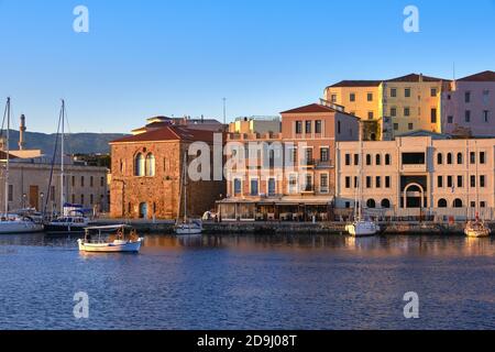 La barca da pesca passa dal Grand Arsenal nel porto vecchio veneziano, la Canea, Creta, Grecia. Vista all'alba su banchina e barche a vela ancorate da moli, caffè. Foto Stock