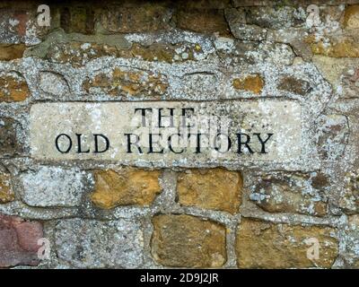 Closeup di 'la vecchia canonica' scolpito casa segno con lettere nere set in vecchio rustico muro di ironstone, Cnossington, Leicestershire, Inghilterra, Regno Unito Foto Stock