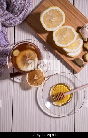 Riscaldare il tè vitaminico con limone e zenzero in una tazza di vetro, fondo bianco. Orientamento verticale. Foto Stock