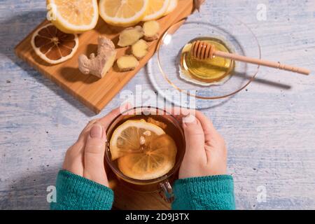 Una tazza di tè caldo con limone, miele e zenzero su una fetta di legno, sfondo chiaro.primo piano. Orientamento verticale. Foto Stock