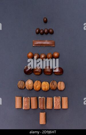 L'albero di Natale è fatto da cioccolato assortito e noci su sfondo nero. Composizione festiva, piatto Foto Stock