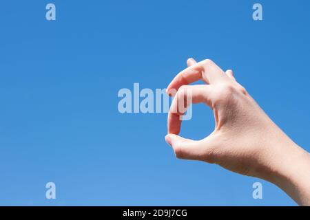 Closeup gesto di una mano donna che fa ok isolato contro uno sfondo blu cielo. Foto Stock