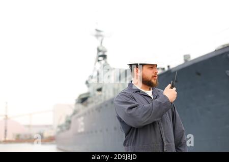 Capitano marino che parla da radio walkie talkie e in piedi vicino nave offshore in pankground. Foto Stock