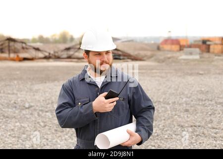 Caposquadra europeo in piedi sul cantiere, parlando da VHF walkie talkie e tenere progetti. Foto Stock