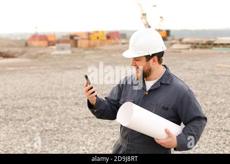 Ingegnere di costruzione maschile americano che tiene VHF walkie talkie e carte in cantiere. Foto Stock