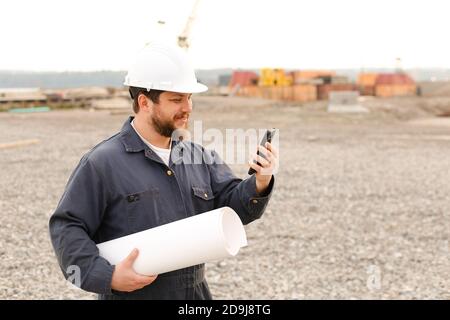 Ingegnere edile americano che tiene VHF walkie talkie e carte in cantiere. Foto Stock