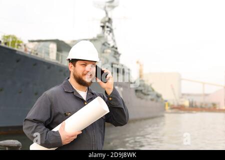 Ingegnere marino che parla da VHF walkie talkie, tenendo carte vicino nave in background. Foto Stock