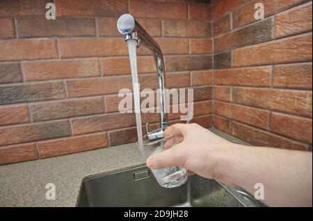 Riempimento di vetro con acqua dal rubinetto casa clsoe in alto vista Foto Stock