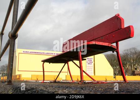 Largs, Ayrshire, Scozia, Regno Unito. Lungomare, con panchine colorate. Una fila di panchine di parco dipinte con colori luminosi lungo il lungomare della località balneare Ayrshire. Contenitori per rifiuti distanziati tra i banchi Foto Stock