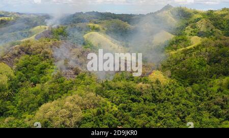 Fuoco di foresta in montagna. Fuoco su colline con vegetazione tropicale. Utilizzare il fuoco per distruggere l'habitat naturale e causare danni ambientali su larga scala in Asia. Bohol, Filippine. Foto Stock