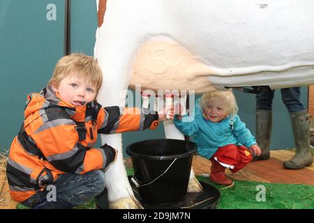 Ayr Agricultural show, Ayrshire, Scozia UK.. Una delle più grandi mostre agricole della Scozia che si tiene all'ippodromo di Ayr. Due bambini provano la loro mano a mungere Foto Stock