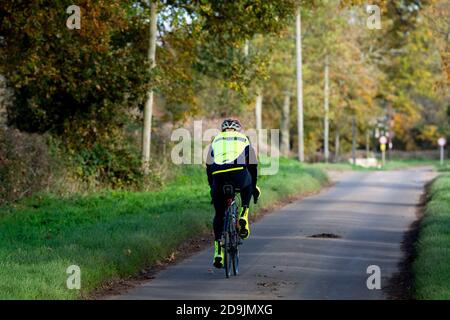 Un ciclista su una strada di campagna in autunno, Sherbourne, Warwickshire, Inghilterra, Regno Unito Foto Stock