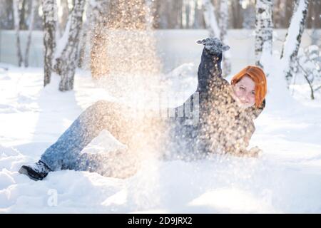 Cute ragazza invita a giocare palle di neve si trova sulla neve nella foresta. Libertà e concetto gioioso. Donna circondata da fiocchi di neve. Foto Stock