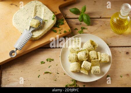 Vista dall'alto della preparazione dei ricci di burro di erbe che mostrano un pat di burro di fattoria con arricciatore e piastra di trucioli completati su un tavolo di legno con erbe a Foto Stock