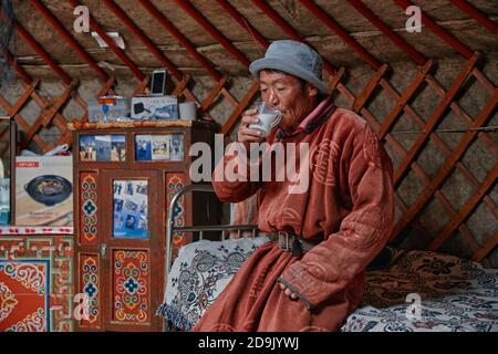 Uomo mongolo in un accappatoio tradizionale, bevendo latte di capra in uno Yurt. Vita dello Yurt mongolo. Interno della casa del nomade. 06.09.2019. Gobi Foto Stock