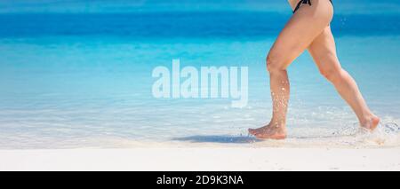 Dettaglio delle gambe della donna che corrono sulla spiaggia. Primo piano di gambe di donna che corrono sulla spiaggia. Donna gambe running, godendo di acqua di spiaggia spruzzi, sabbia bianca Foto Stock