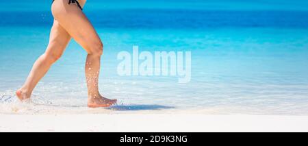 Dettaglio delle gambe della donna che corrono sulla spiaggia. Primo piano di gambe di donna che corrono sulla spiaggia. Donna gambe running, godendo di acqua di spiaggia spruzzi, sabbia bianca Foto Stock