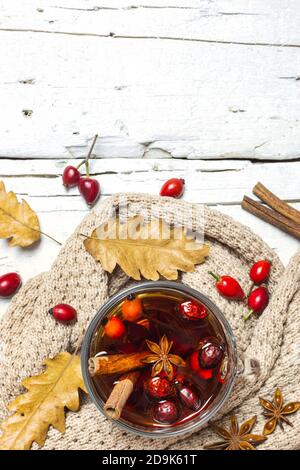 Foto ravvicinata di una tazza di tè con rose e spezie, abiti caldi, foglie essiccate su rustico sfondo in legno, vista dall'alto. Concetto autunnale. Foto Stock