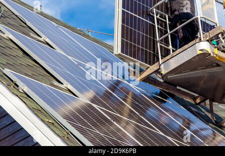 Lavoratori che installano pannelli solari su casa privata tetto esagonale feltro in giornata di sole, cielo blu. Vita reale. Centrale elettrica domestica. Foto Stock