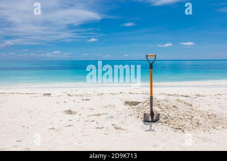 Pala in sabbia alla spiaggia. Immagine grandangolare di una pala nella sabbia su una spiaggia sotto un cielo blu parzialmente nuvoloso. Foto Stock