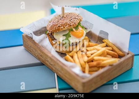 Hamburger e patatine fritte. Hamburger gigante con patatine fritte in piatto di legno. Hamburger gourmet fatto in casa nel tavolo ristorante all'aperto Foto Stock