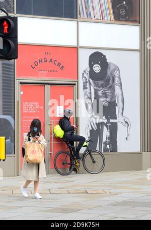 Londra, Inghilterra, Regno Unito. Ciclista e donna asiatica che guardano i loro telefoni cellulari a Covent Garden Foto Stock