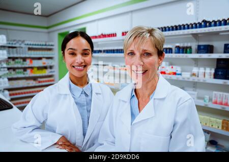 Donna caucasica farmacista sorridente con assistente di razza mista in piedi dietro banco in farmacia Foto Stock