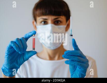 Un'infermiera femminile indossa guanti di gomma e indossa una maschera medica per il viso, un medico femminile tiene una siringa e un vaccino COVID-19, fondo bianco isolato, Foto Stock